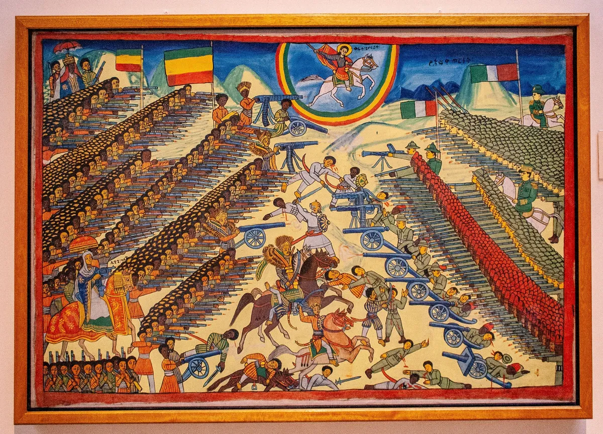 A crowded painted battle scene: rows of Ethiopian soldiers facing Italian troops and artillery, with a mounted saint in a halo above.