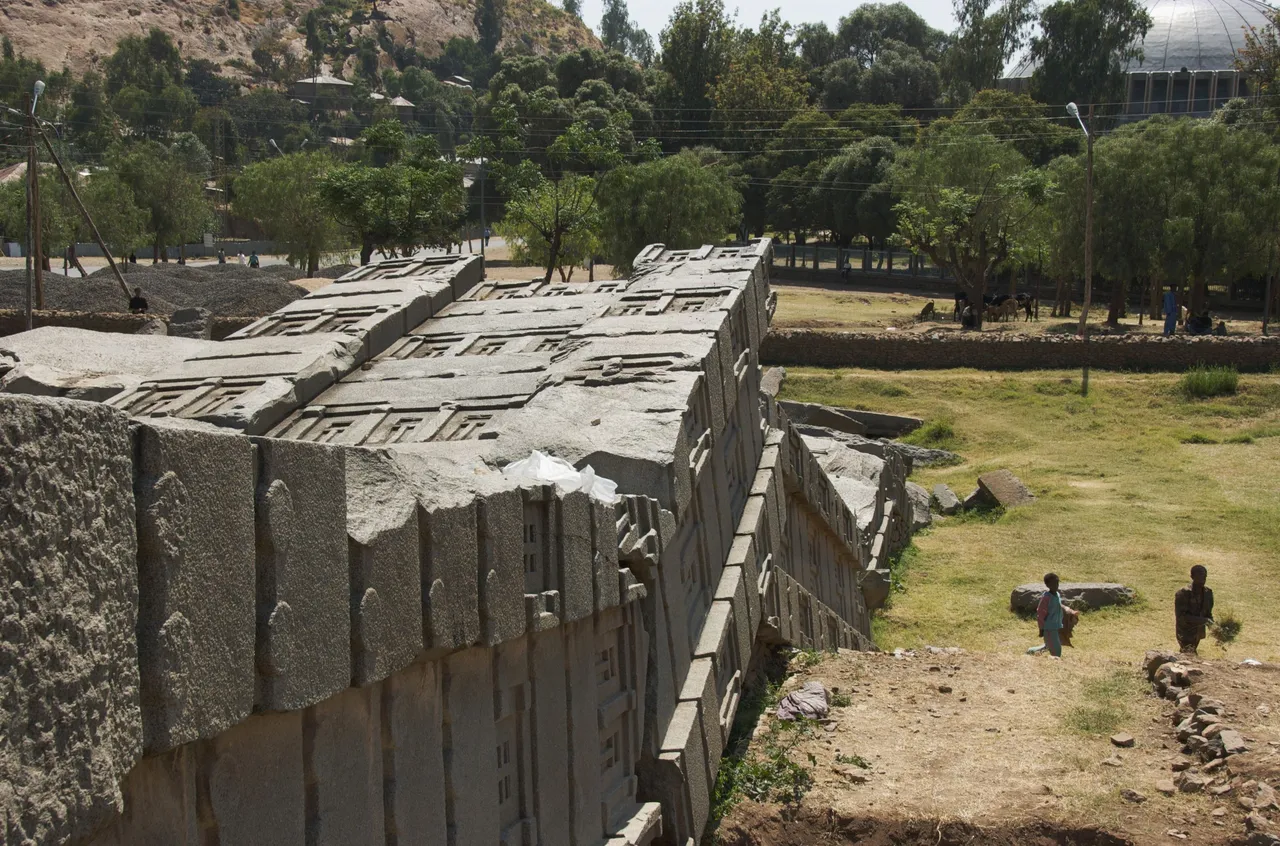 A huge broken granite stela lying on the ground among trees.