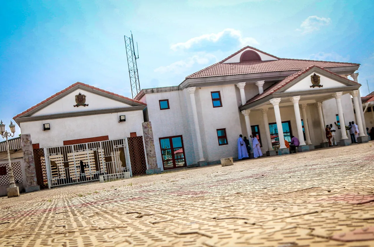 A white palace building with columns and red-tiled roofs behind a paved forecourt.