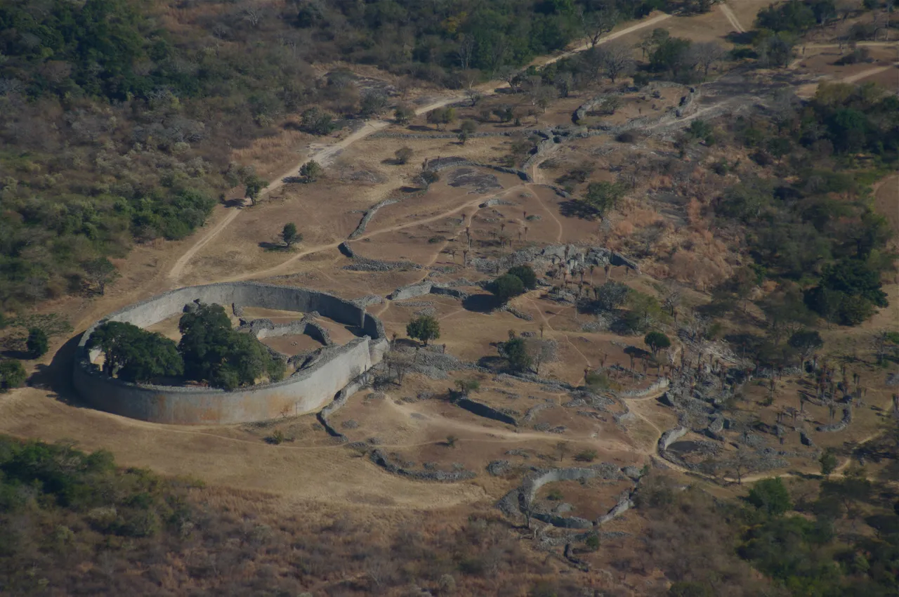 Curving dry-stone walls of a great enclosure in a wooded valley, seen from a hilltop.