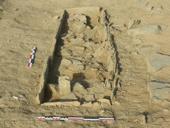 A cleared burial on open stony ground with a single upright slab standing at its head.