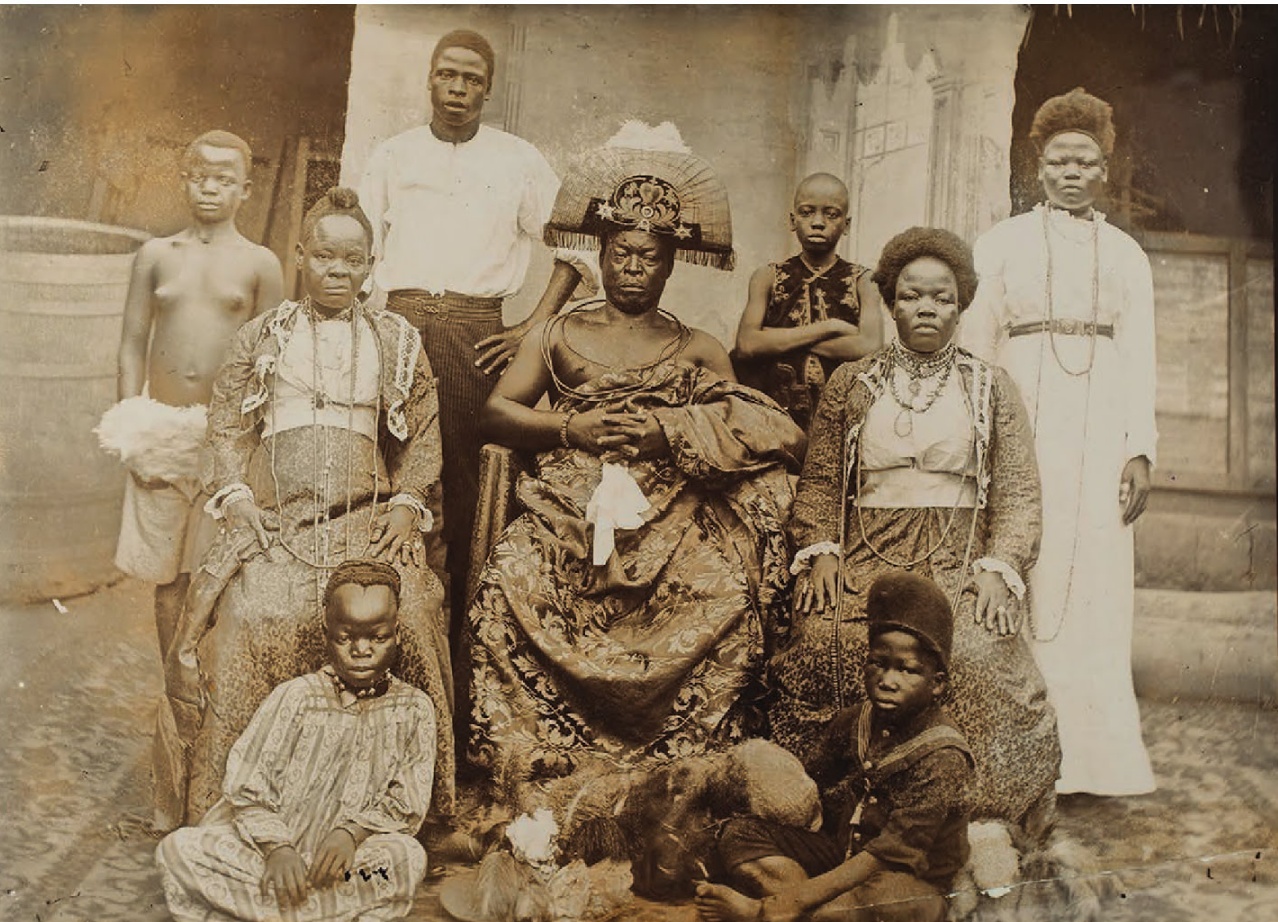A group portrait of a seated older man in a wrapped cloth, with women and children standing and sitting around him.